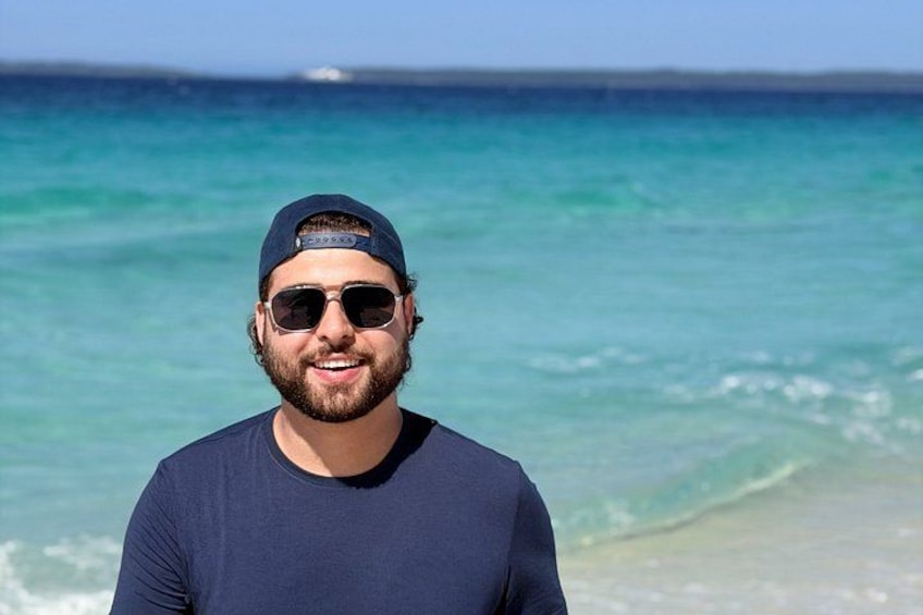 A person standing on a beach with a clear blue sea in the background. 3