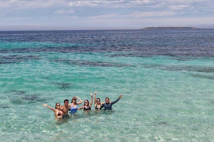 A group of people in clear turquoise water, with a distant landmass on the horizon. 2