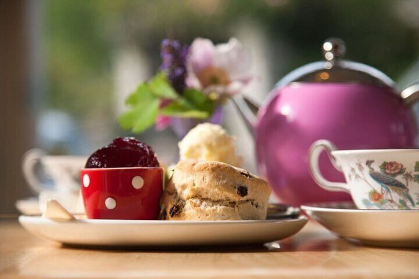 A plate with a red mug, a biscuit, and a teapot on a table. 5
