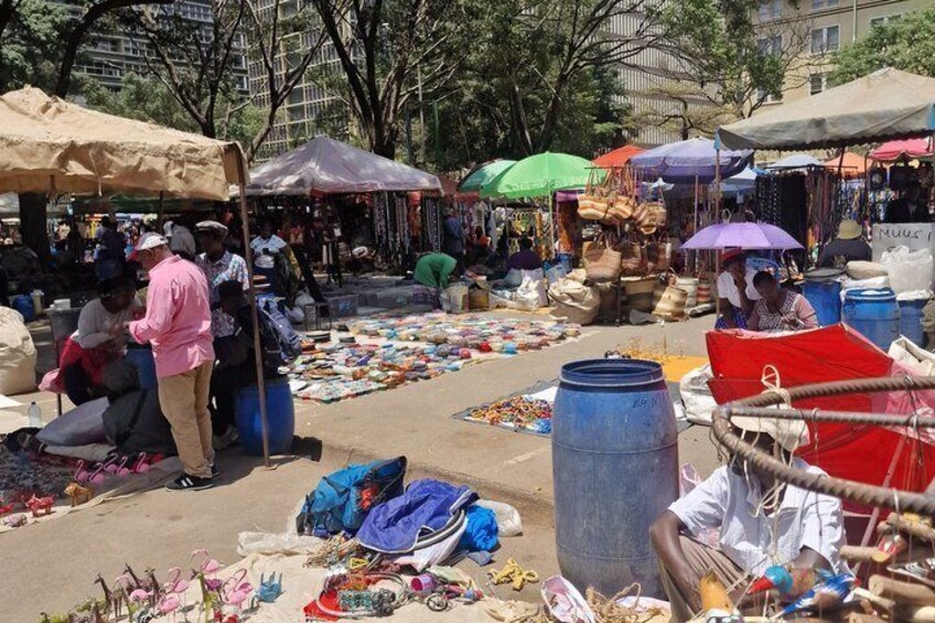 A bustling outdoor market with various stalls selling goods, people browsing, and umbrellas providing shade. 5