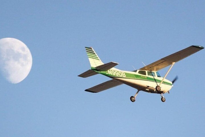 Un pequeño avión con la matrícula N990B volando contra un cielo despejado con la luna de fondo. 2