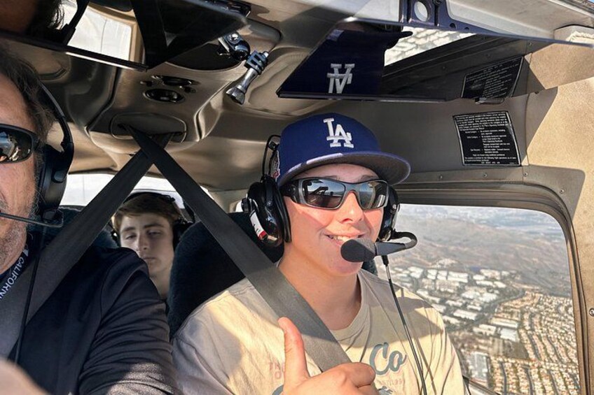 En person i en pilotstol med headset, mikrofon og LA-kasket. 1