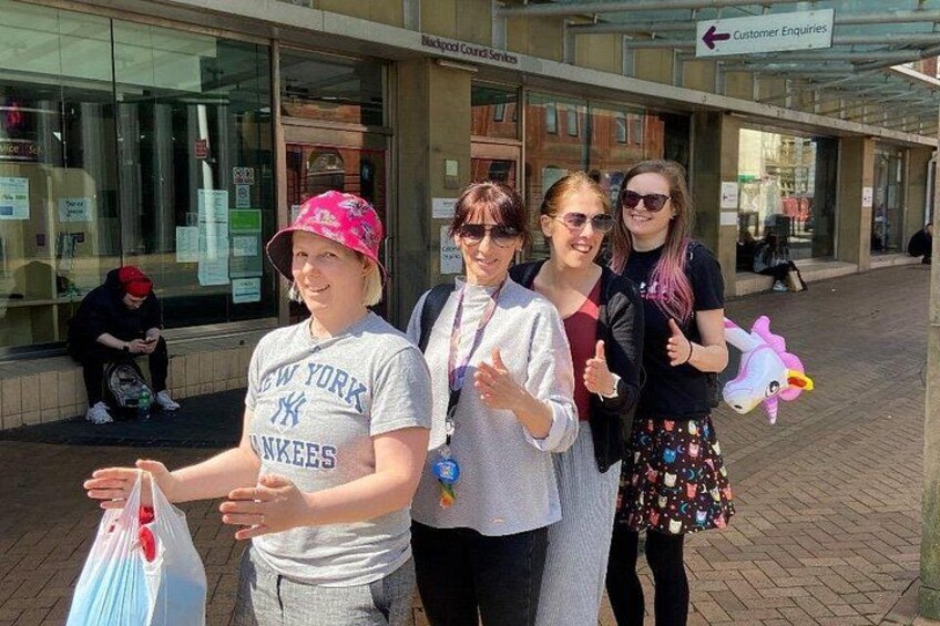 Four people standing on a sidewalk, one holding a bag. 3