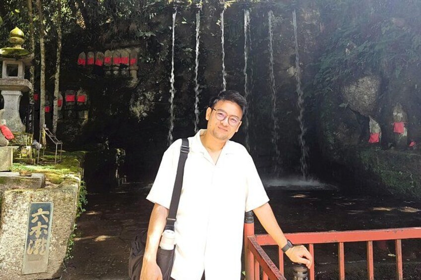 A man standing near a waterfall with a stone structure and a red railing. 3