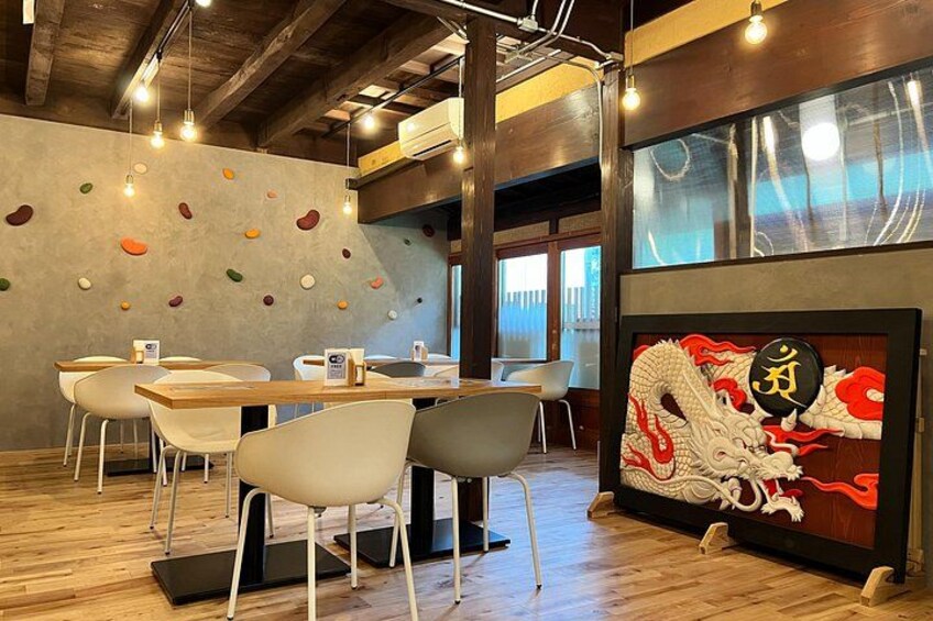 A restaurant interior with wooden tables, white chairs, a dragon mural, and a concrete wall with colorful pebbles. 5