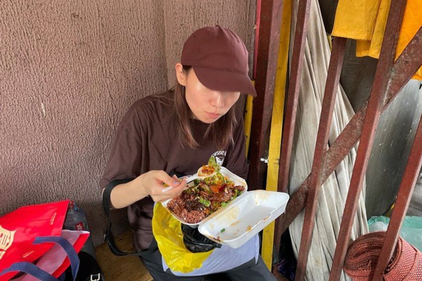 Una persona sentada al aire libre, sosteniendo un recipiente con comida. 4
