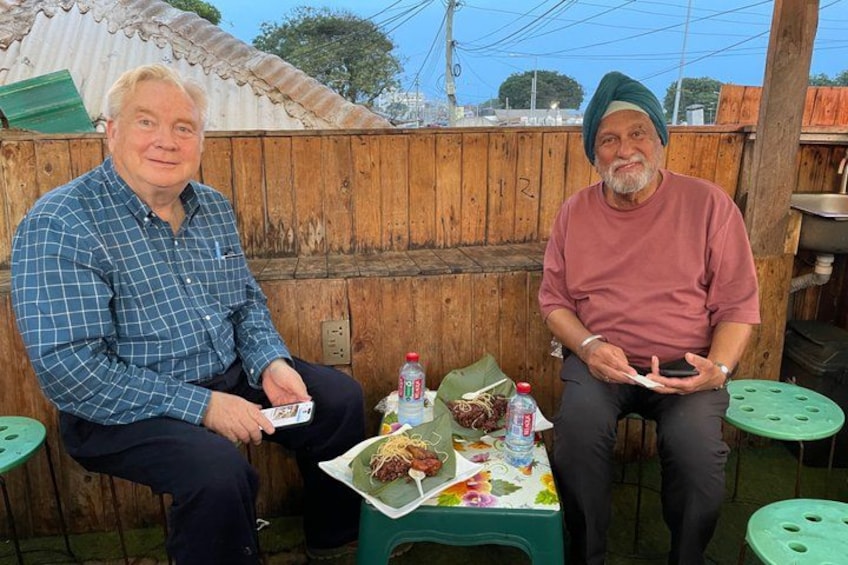 Dos hombres sentados en una mesa con comida y bebidas. 2