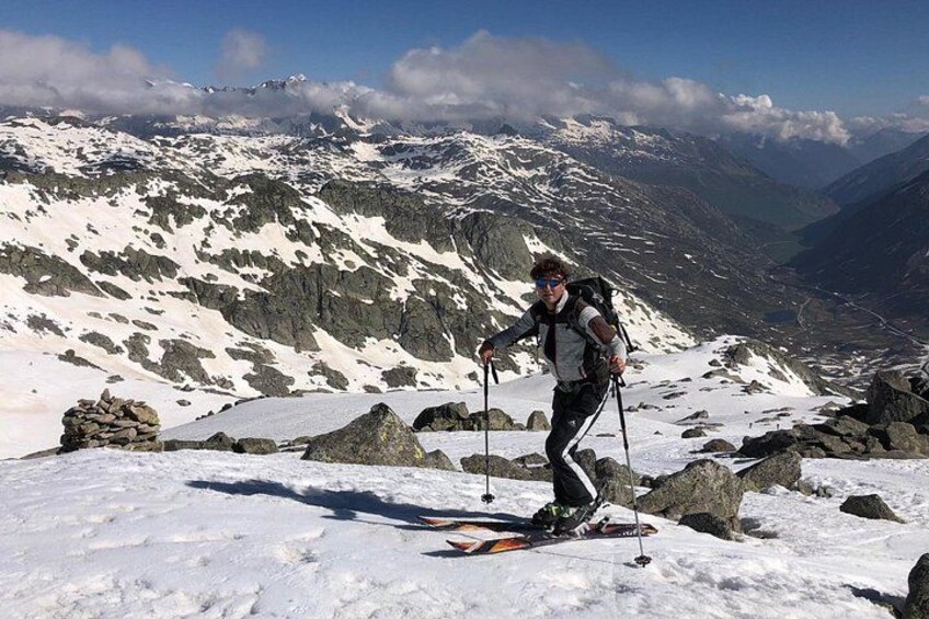 Eine Person wandert auf einem mit Schnee bedeckten Berg mit felsigem Gelände und weit entfernten, schneebedeckten Gipfeln. 1