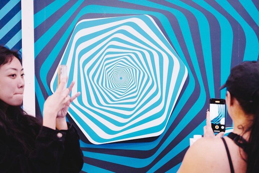 A person taking a photo of a geometric art installation with concentric hexagonal patterns. 4