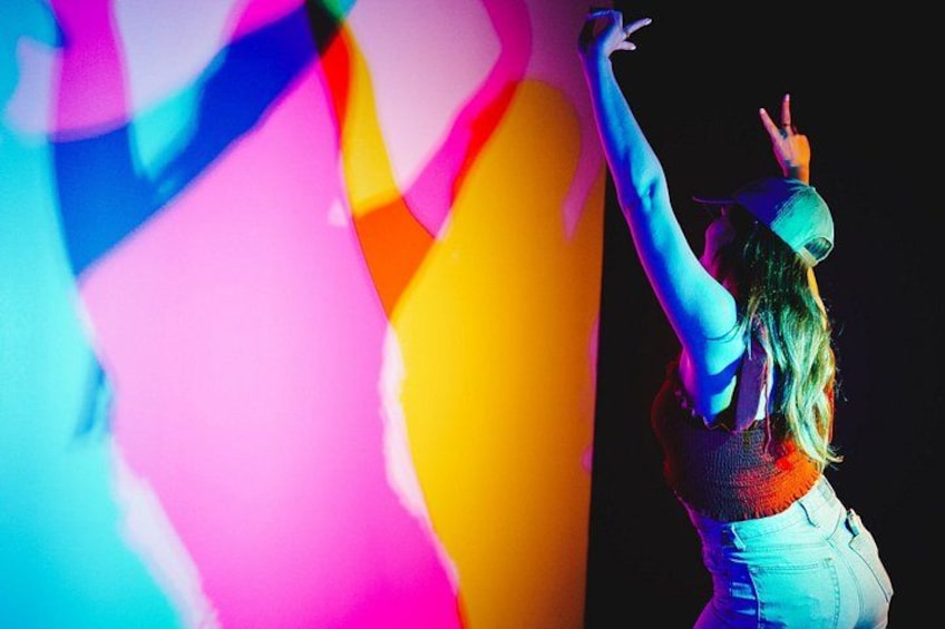 A person with raised arms, wearing a cap and a sleeveless top, in a brightly lit environment with colorful lighting effects. 5