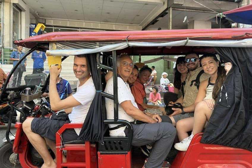 A group of people on a red three-wheeled vehicle with a canopy, parked in an urban setting. 3