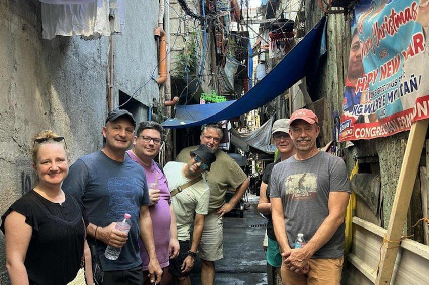 A group of people standing in a narrow alleyway with a blue tarp overhead and a banner on the right. 4