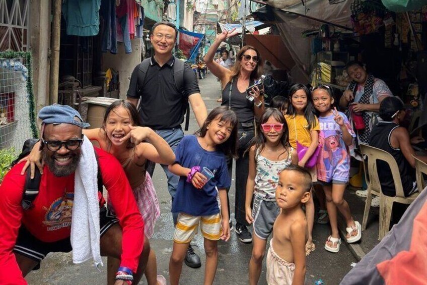 En gruppe mennesker udendørs, nogle i afslappede klæder, med et provisorisk ly i baggrunden. 1