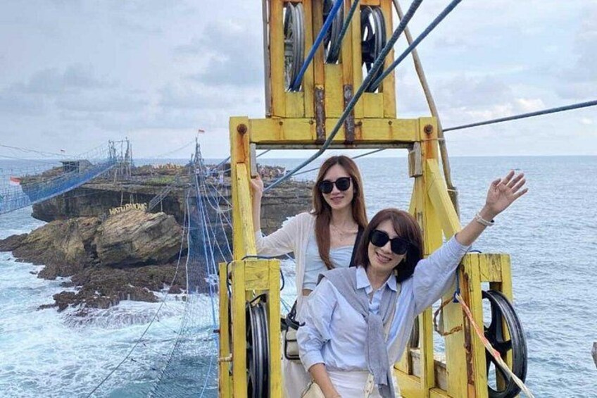 Deux personnes se trouvent dans une cabine de téléphérique jaune. On aperçoit, en arrière-plan, une côte rocheuse et un pont suspendu. 5