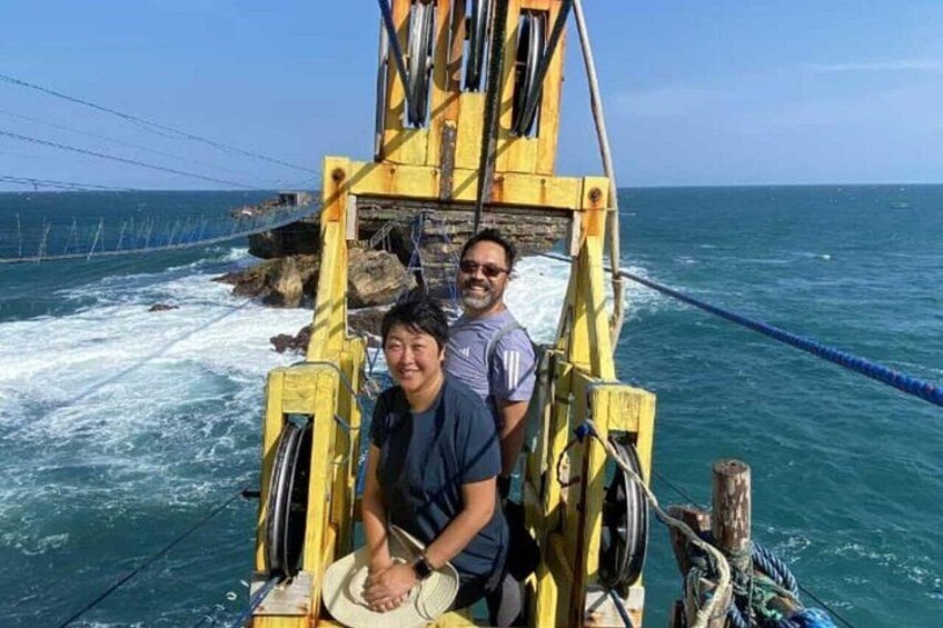 Deux personnes se trouvent dans un bateau jaune, des cordes sont visibles, et on aperçoit des vagues de l’océan ainsi qu’une côte rocheuse en arrière-plan. 3