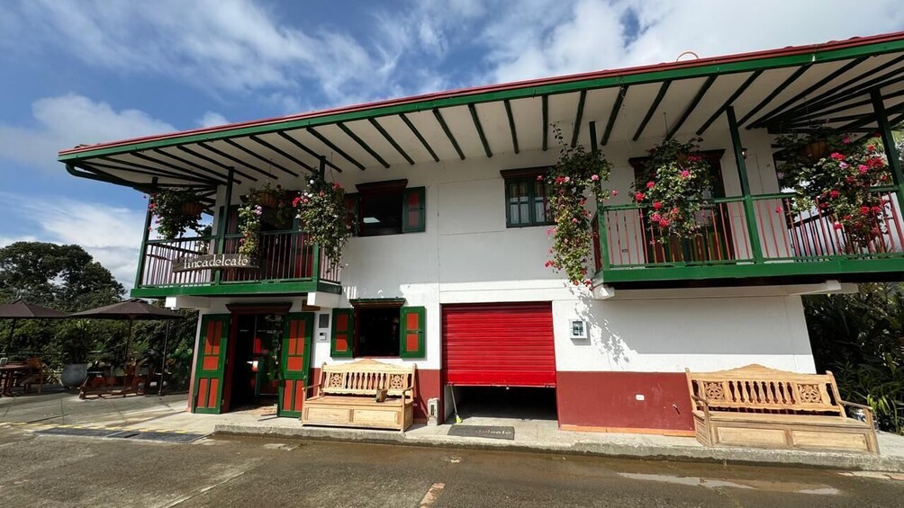 Un edificio de dos pisos con fachada verde y blanca, balcones adornados con flores colgantes y una puerta de garaje roja. 1