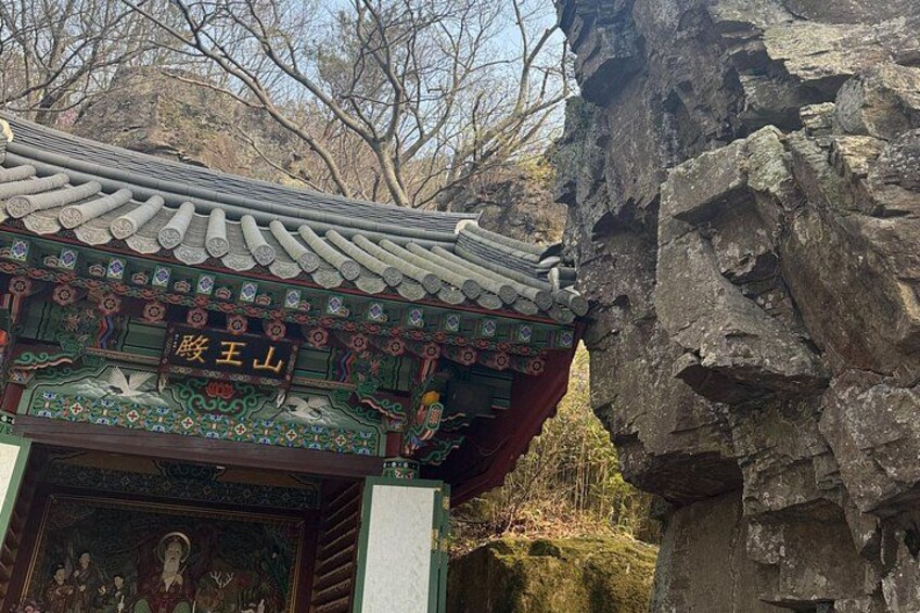 Un templo coreano tradicional con arquitectura ornamentada, una formación rocosa y un telón de fondo montañoso. 4