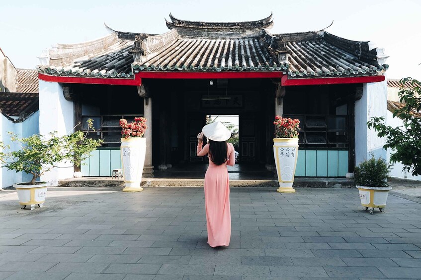A woman in a pink dress standing in front of a traditional Chinese gate with a red roof and white columns. 5
