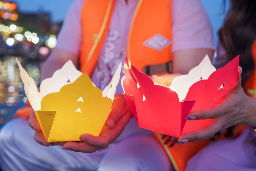 Two people holding paper lanterns, one yellow and one red, with a cityscape in the background. 4