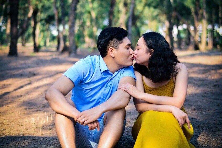 A couple sitting on the ground in a park with trees in the background. 1