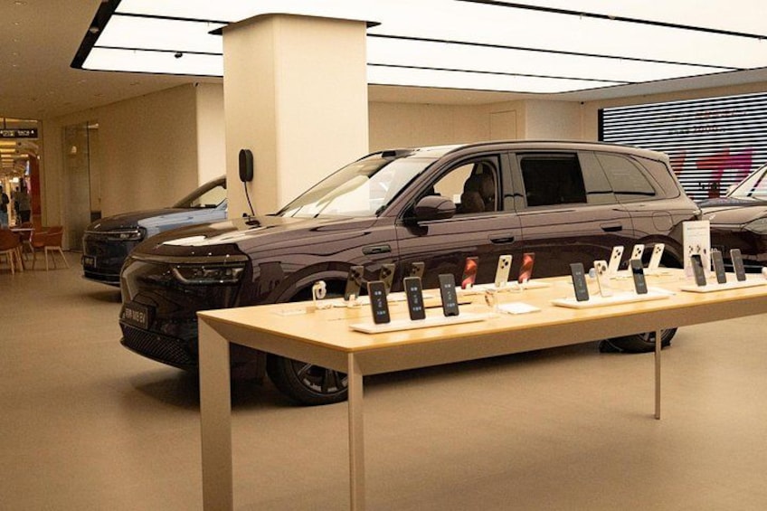 A showroom with a display table of electronic devices and two cars. 5