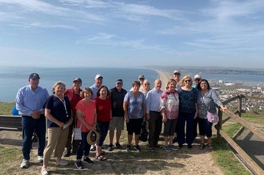 A group of people standing on a grassy hill overlooking a coastal landscape with a clear sky. 1