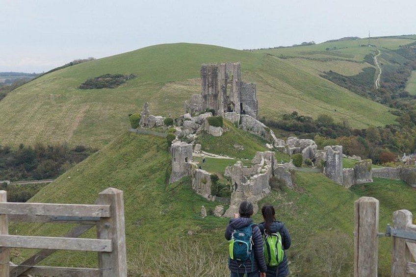 A historic stone castle ruins on a grassy hill with a wooden fence in the foreground. 2