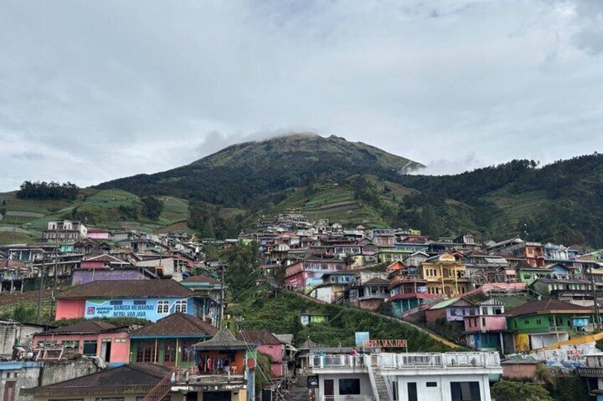 Un pueblo en la ladera de una colina con casas coloridas y una montaña al fondo. 2