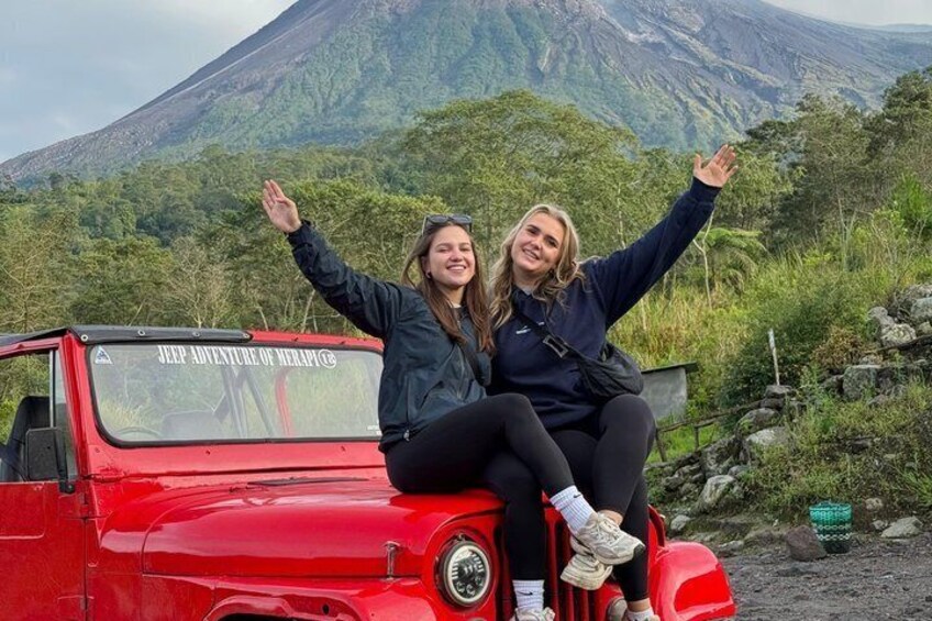 Dos personas sentadas en un Jeep rojo, con un paisaje montañoso al fondo. 1