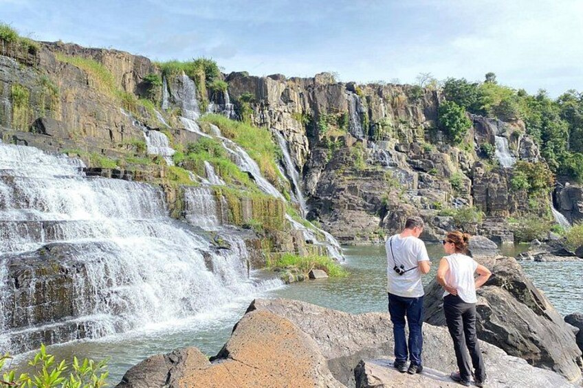 Ett vattenfall som störtar ner över klippor och ut i en flod, omgivet av grönska och branta klippor. 2