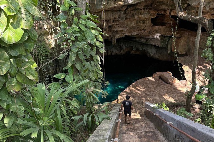 A person walking on a stone bridge over a cave entrance with a clear blue pool below. 4