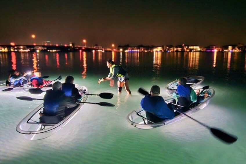 People kayaking on calm water at night with city lights in the background. 1