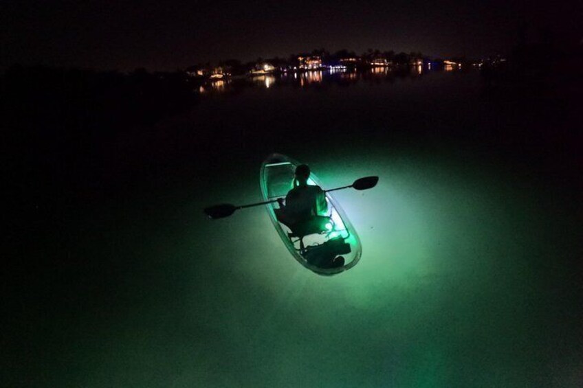 A kayak with a green light on a calm body of water at night. 2