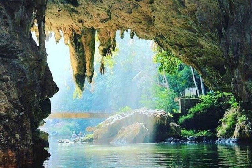 Eingang einer Höhle mit Stalaktiten, einem ruhigen Fluss und üppiger Vegetation. 5