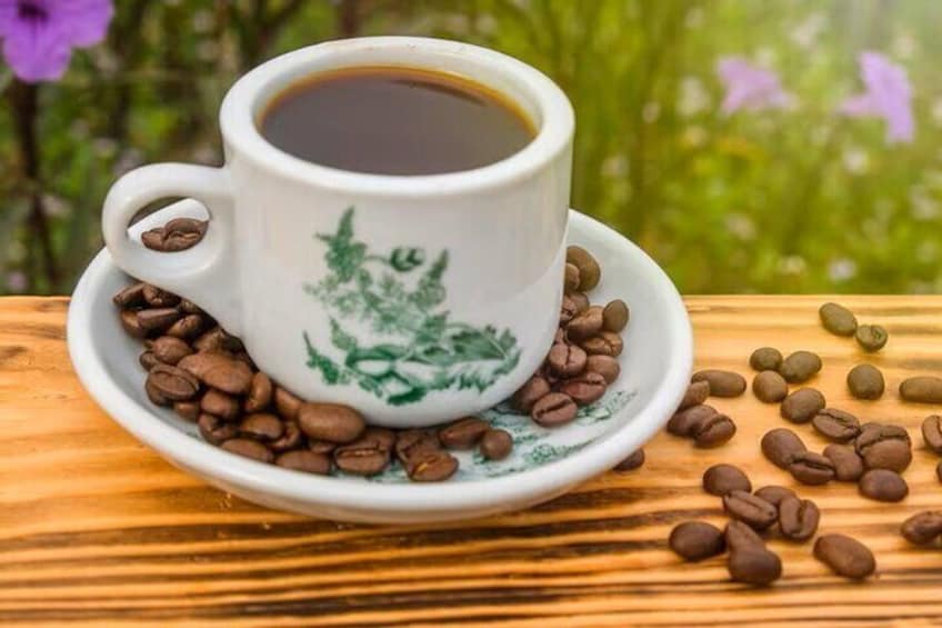 A white ceramic cup with green floral designs, filled with coffee, surrounded by coffee beans on a wooden surface. 1