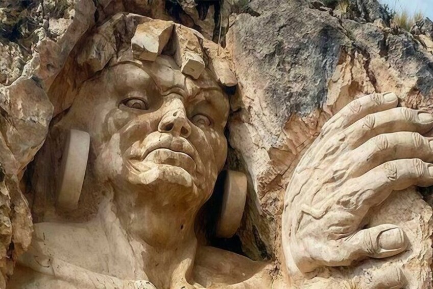 Un gran rostro tallado en piedra con una mano que asoma de la roca. 2