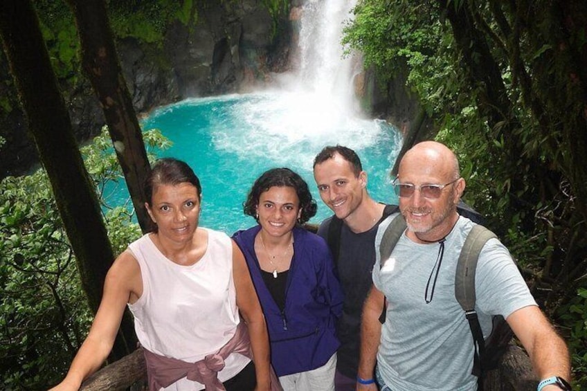 A group of people standing in front of a waterfall with lush greenery in the background. 1