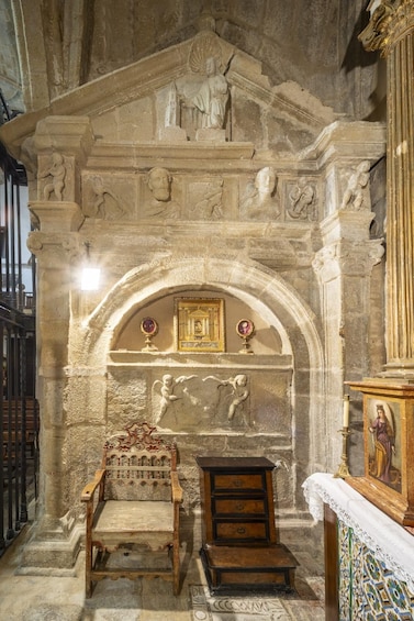 An ornate stone archway with religious carvings and a wooden chair. 3