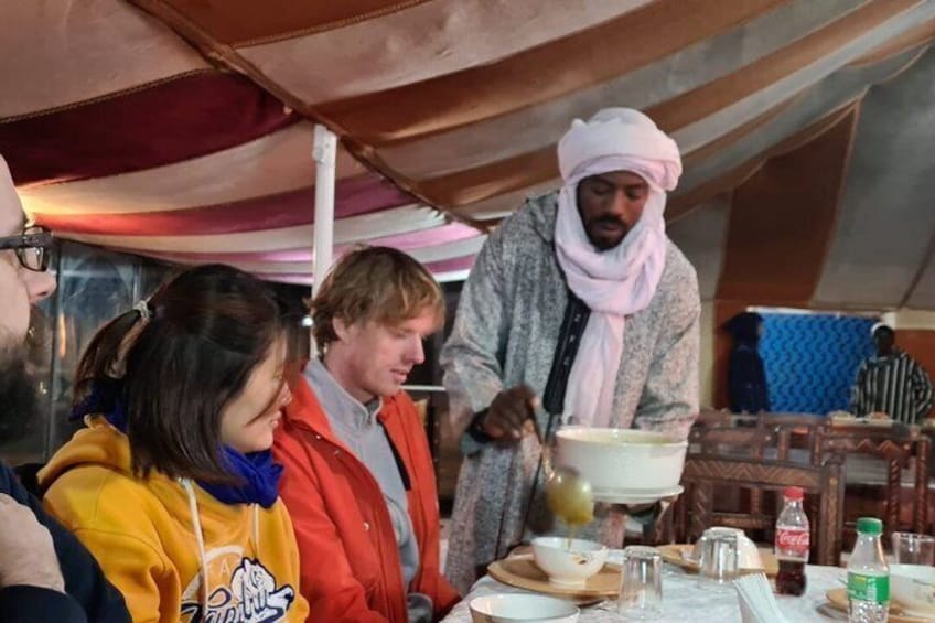 A group of people around a table with food and drinks, under a tent. 3