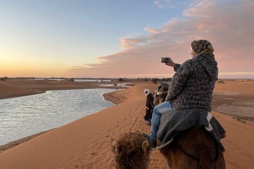 A person riding a camel along a riverbank in a desert landscape. 2