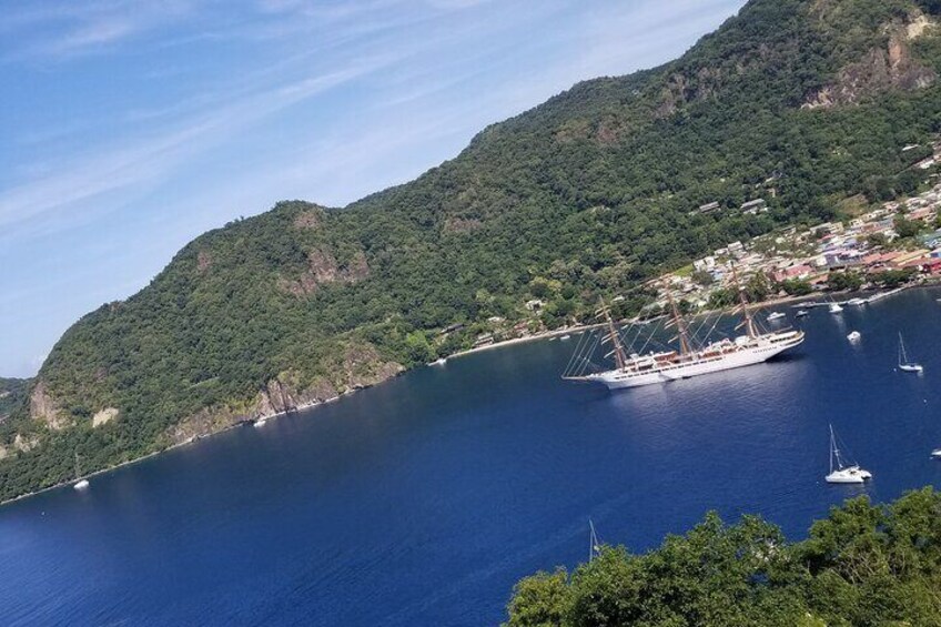 A large body of water surrounded by green hills, with a sailboat anchored near the shore. 2