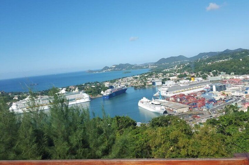 A coastal city with a large cruise ship docked at a port, surrounded by lush greenery and hills in the background. 1