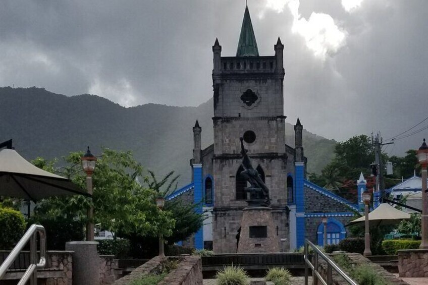 A historic church with a bell tower and statue, surrounded by lush greenery and mountains. 5