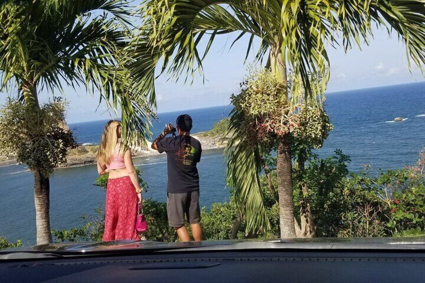A man taking a photo of a woman near a body of water with palm trees and a clear sky in the background. 4