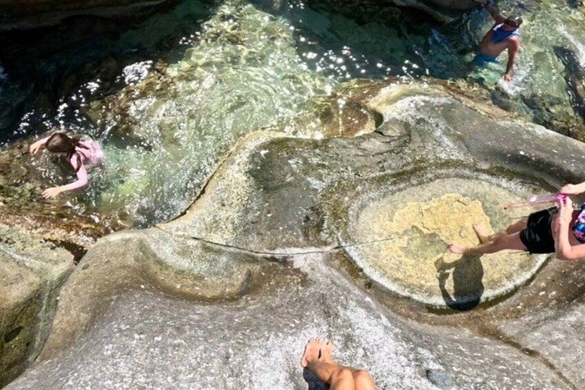 People swimming in a natural pool with clear water and rocky formations. 3