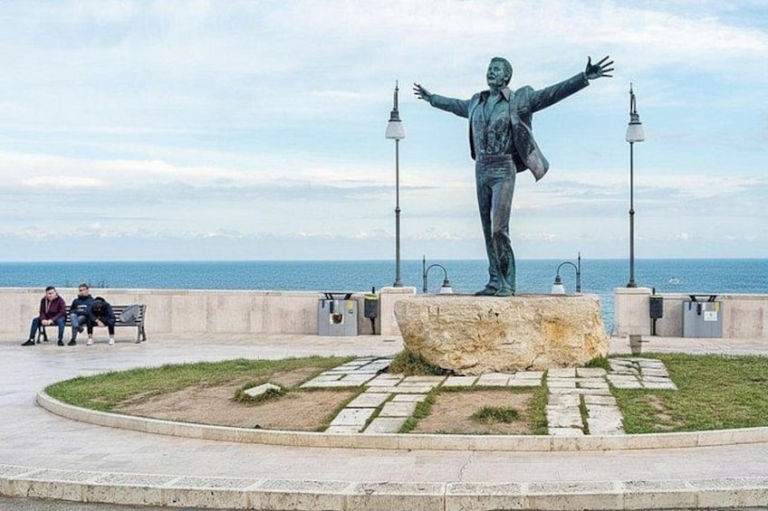 A statue of a man with arms outstretched, a circular stone platform, and a bench with two people sitting. 3