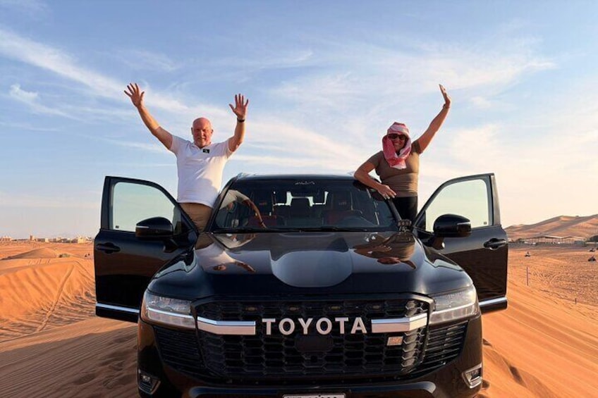 A black Toyota truck in a desert with two people standing on the hood, one with arms raised. 1