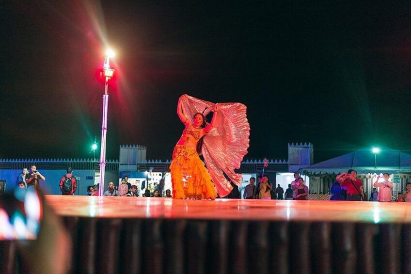 A person in a flowing orange costume performing on a stage with a crowd in the background. 4