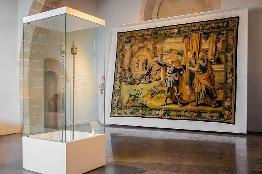 Een glazen displaykast met een sculptuur, een groot schilderij met figuren, en een klassiek gebouw op de achtergrond. 2
