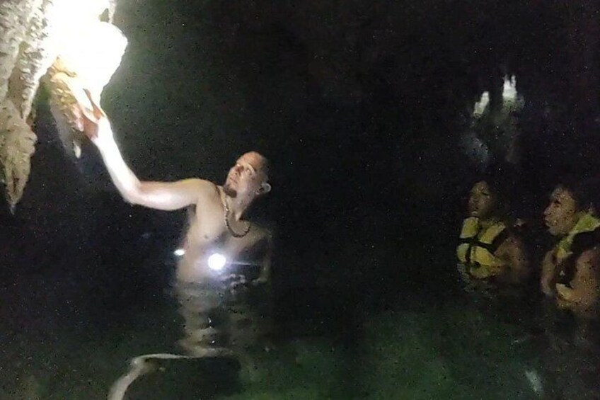 Une personne qui tend la main vers l’entrée d’une grotte, une autre personne dans l’eau et l’ouverture de la grotte. 2